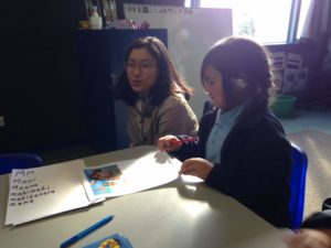 Teacher crouches beside child at school desk 